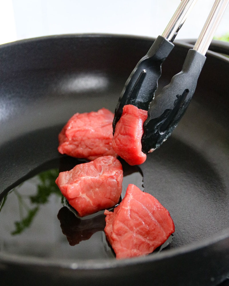 Dieses Bild zeigt wie das Fleisch in die Pfanne gegeben wird.