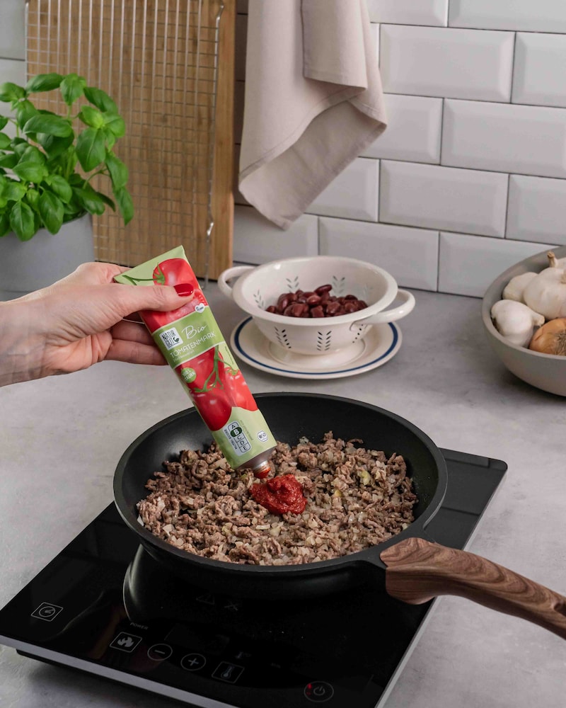 Dieses Bild zeigt wie das Tomatenmark zum Hackfleisch gegeben wird.