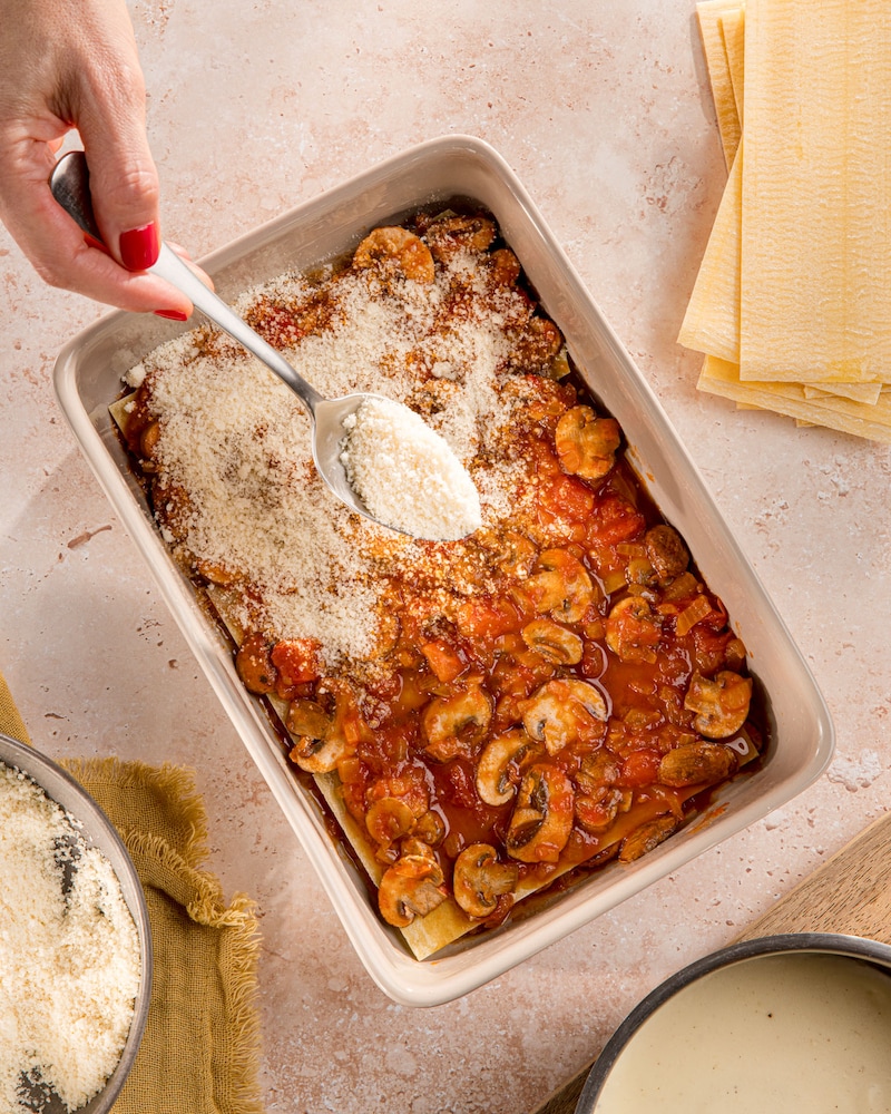 Dieses Bild zeigt wie die Lasagne mit Käse bestreut wird.