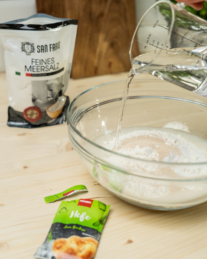 Auf diesem Bild siehst du wie Wasser, Mehl und Hefe in einer Schüssel verrührt werden.