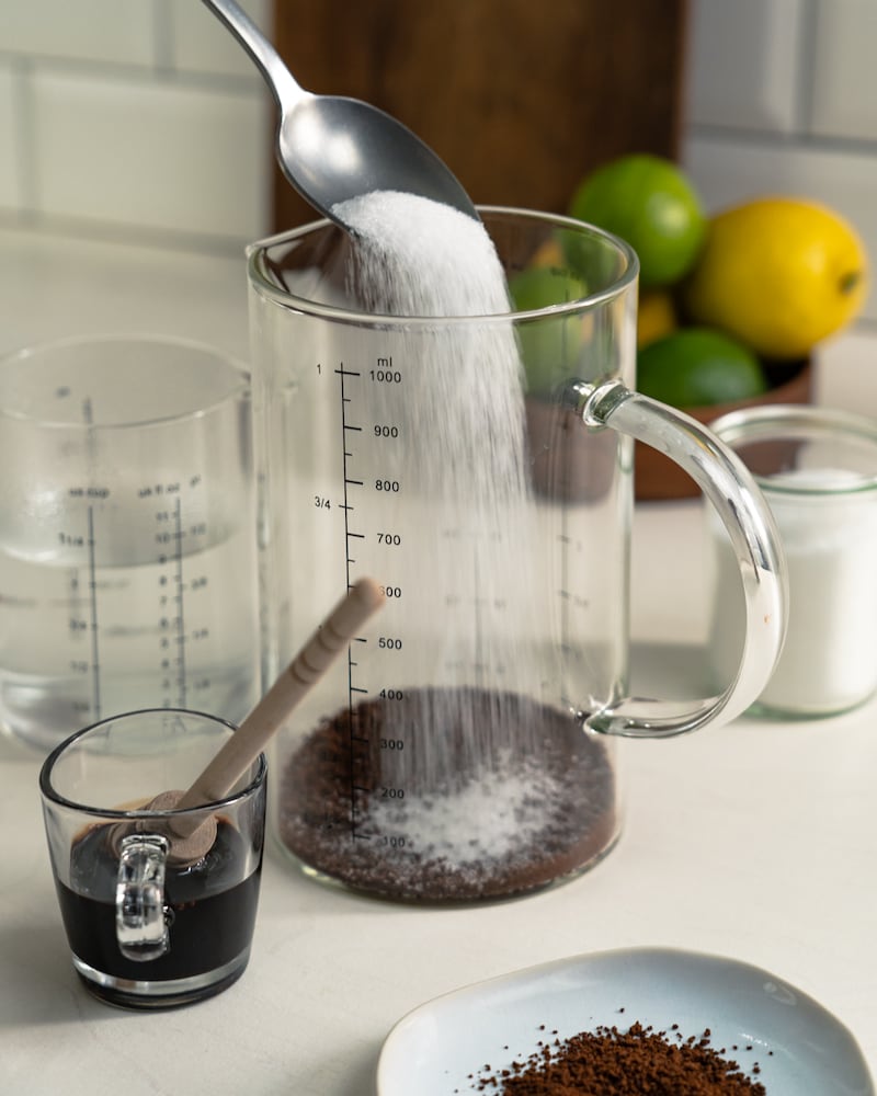 Auf diesem Bild siehst du wie Zucker und Kaffeepulver in einen Messbecher gegeben werden.