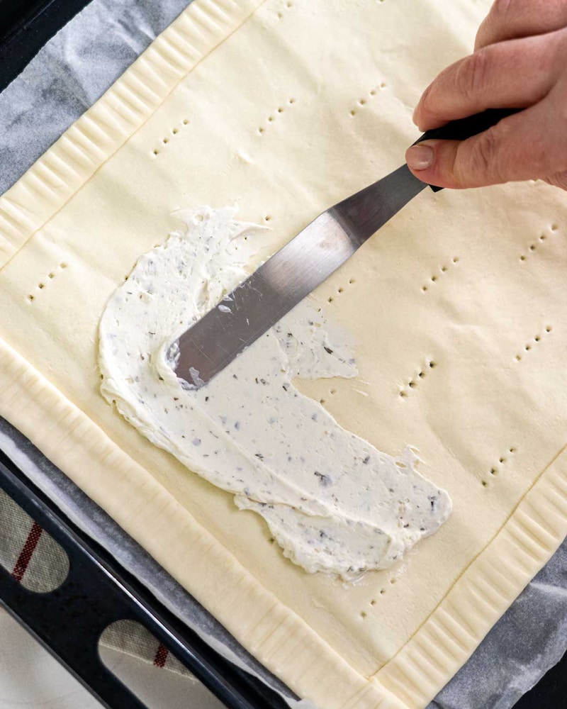 Auf diesem Bild siehst du wie der Teig mit Frischkäse bestrichen wird.