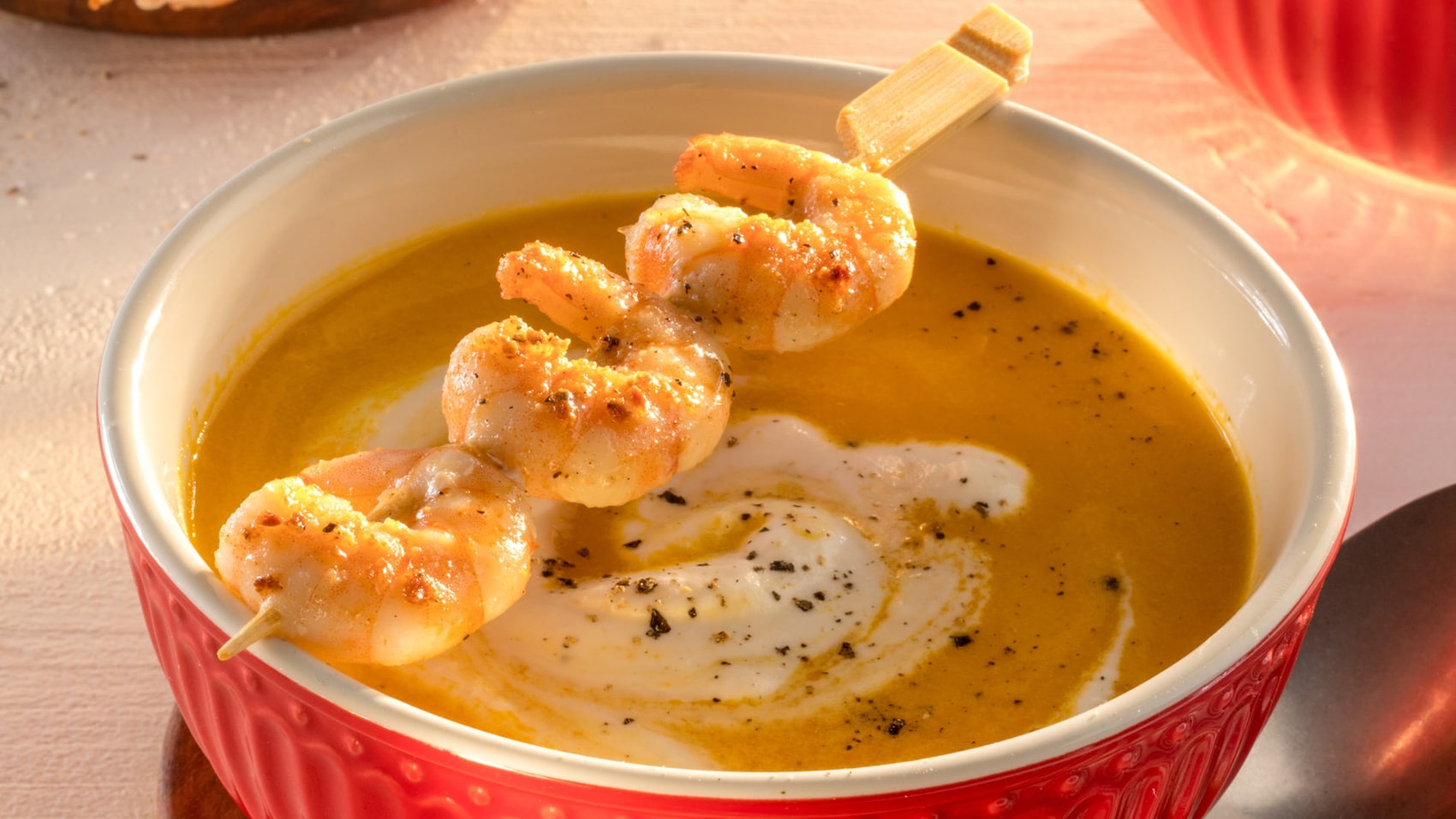 Karotten-Orangen-Suppe mit Garnelen in einer roten Schüssel
