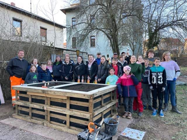 Kinder und Vereinsmitglieder laecheln stolz neben ihren neuen Hochbeeten