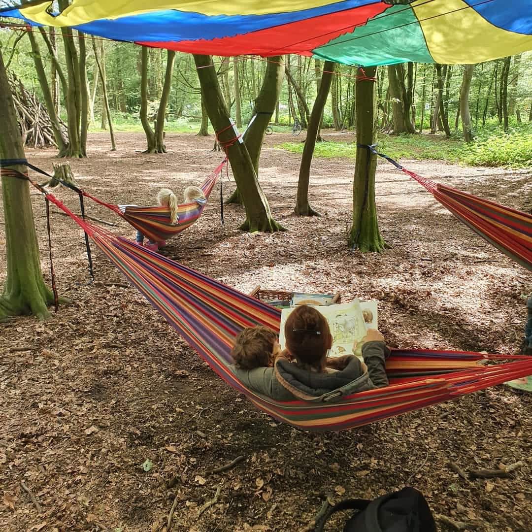 Kinder und Erwachsene liegen in Haengematten im Wald