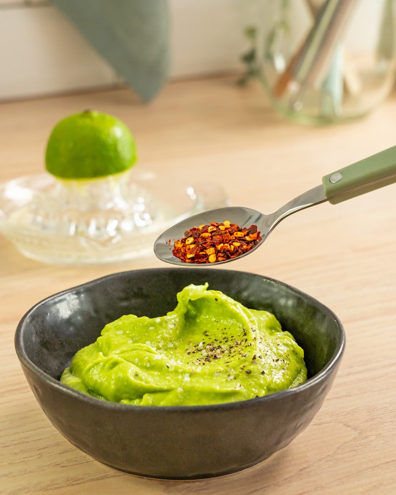 Dieses Bild zeigt wie Chiliflocken über die Avocadomasse gegeben werden.