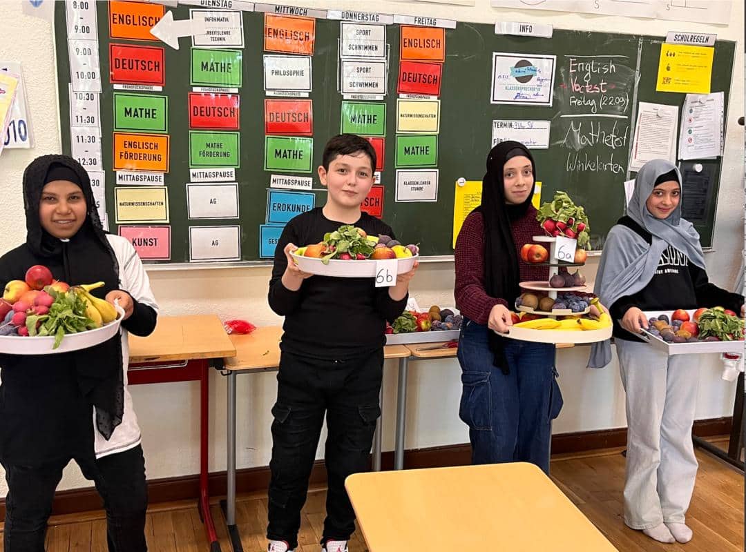 Kinder zeigen grosse Platten mit Obst und Gemuese