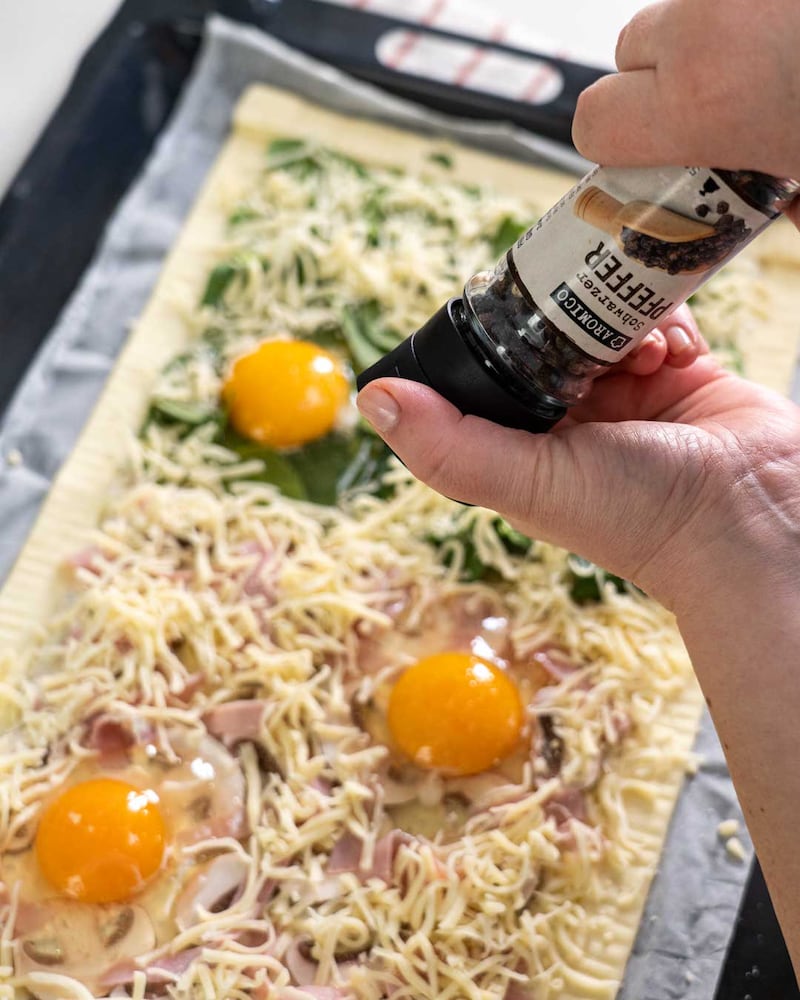 Auf diesem Bild siehst du wie die Pizza mit Pfeffer gewürzt wird.