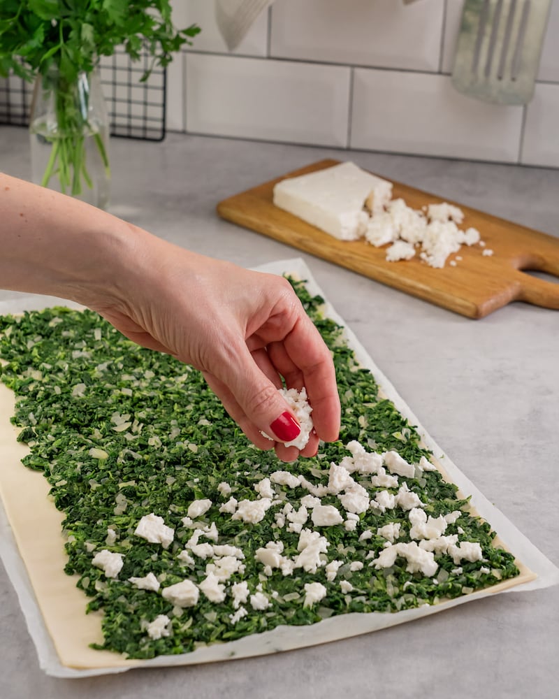 Dieses Bild zeigt wie Feta auf dem Spinat verteilt wird.