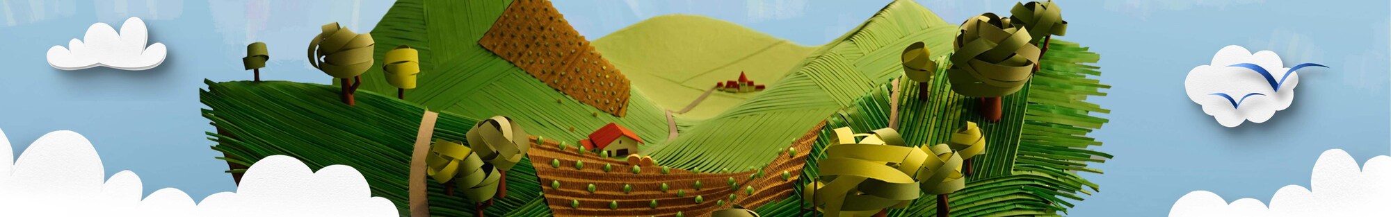 Eine idyllische Landschaft mit landwirtschaftlichen Feldern, Wiesen, Bergen, einem kleinen Ort im Hintergrund und Wolken am Horizont vor hellblauem Himmel.