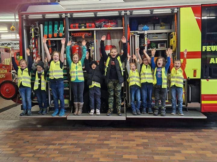 Kinder am Feuerwehrwagen strecken froehlich ihre Haende in die Hoehe
