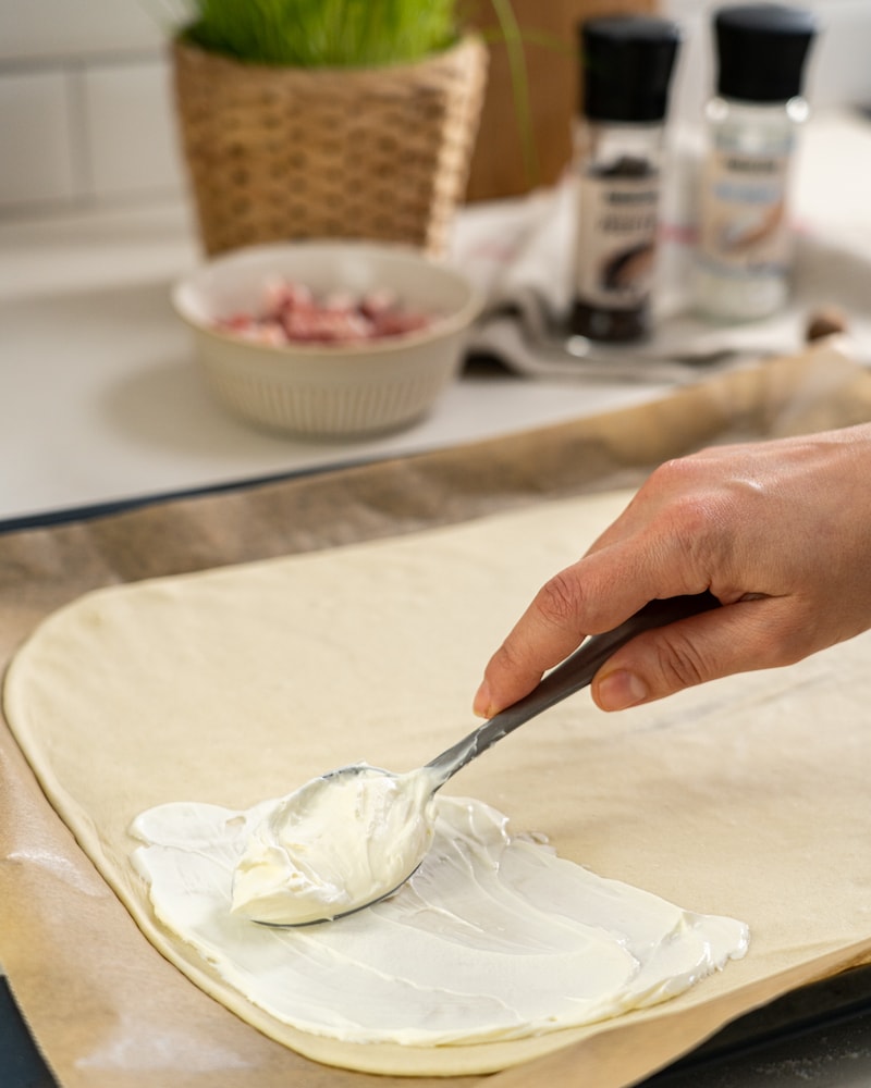 Das Bild zeigt wie der Teig mit Creme Fraiche bestrichen wird.