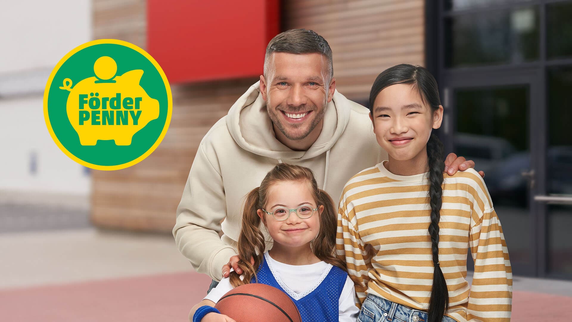 Lukas Podolski mit zwei Kindern und dem Förderpenny-Logo