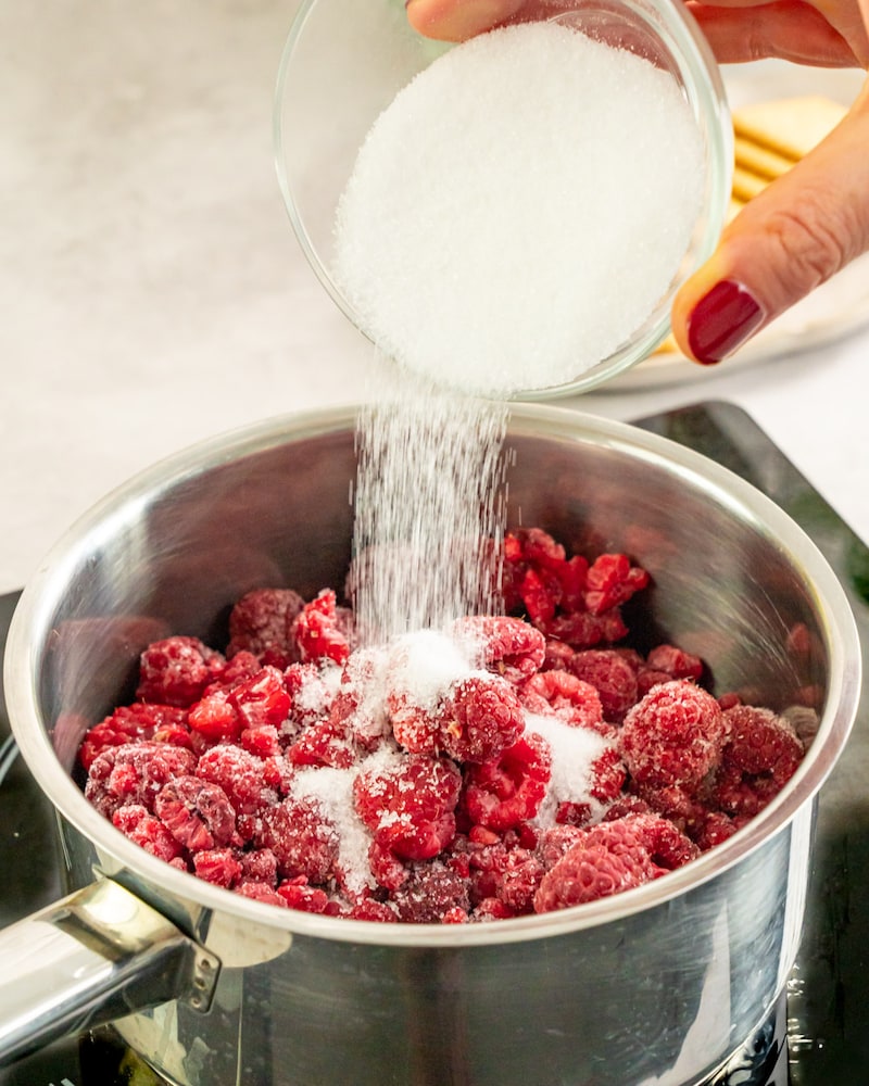Dieses Bild zeigt wie Zucker über Himbeeren in einem Topf gegeben wird.