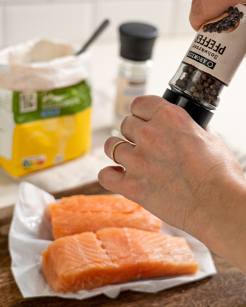 Auf diesem Bild siehst du wie die Lachsfilets gepfeffert werden.