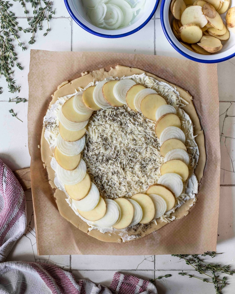 Dieses Bild wie die Kartoffeln und Zwiebeln auf die Galette gegeben wird.