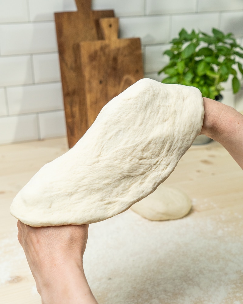 Auf diesem Bild siehst du wie der Teig in eine Pizza geformt wird.