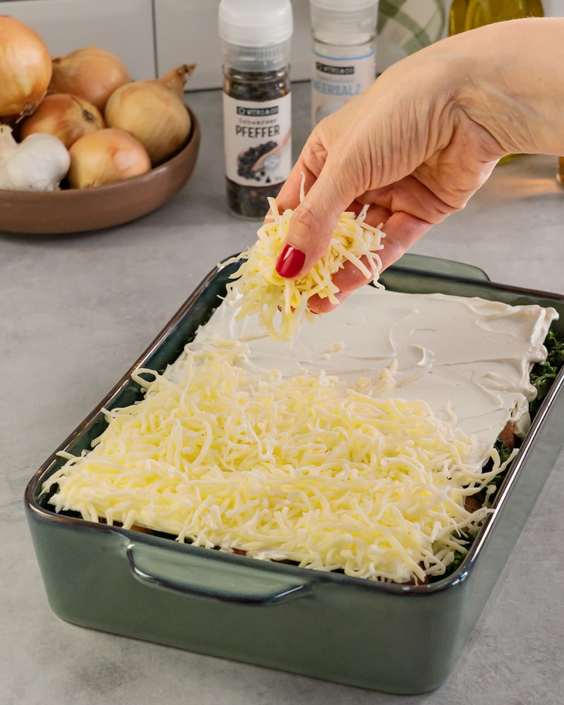 Dieses Bild zeigt wie die Lasagne mit Käse bestreut wird.