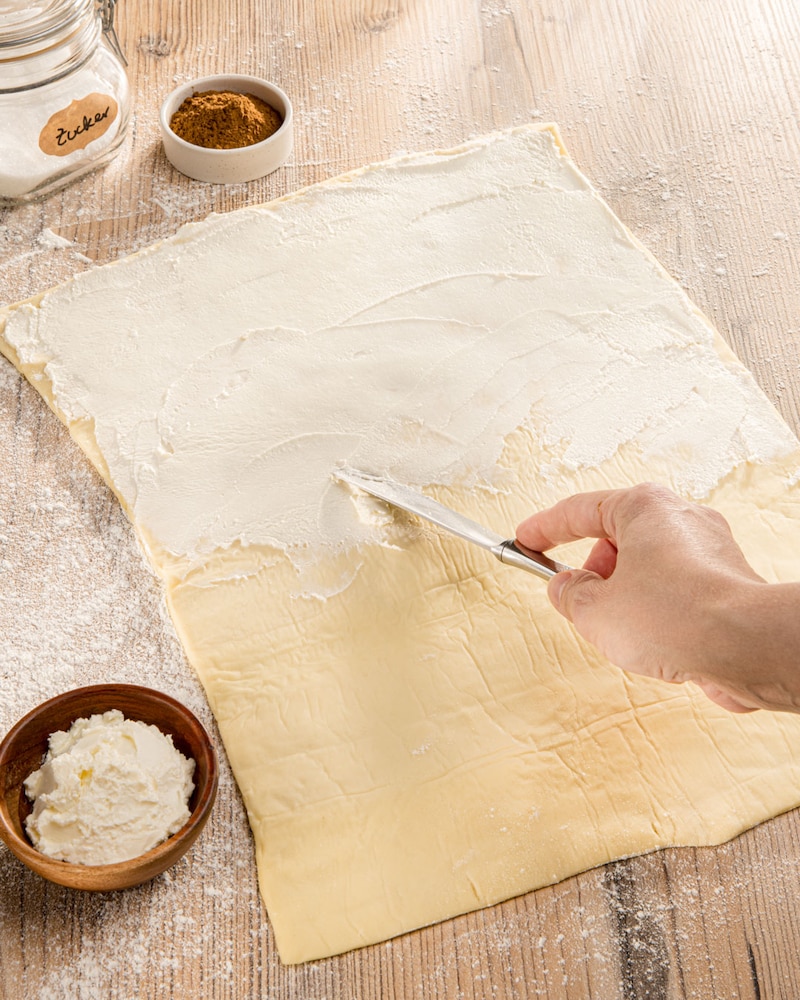 Dieses Bild zeigt wie der Pizzateig mit Frischkäse bestrichen wird.