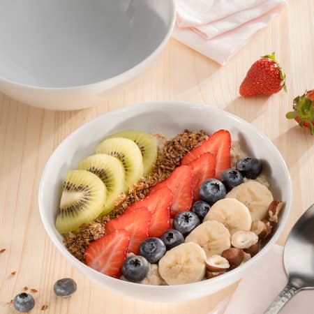 Dieses Bild zeigt eine Müslischale mit Kiwi, Erdbeeren, Heidelbeeren, Bananen, und Nüssen.