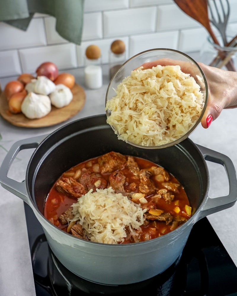 Auf diesem Bild siehst du wie das Sauerkraut dazugegeben wird.