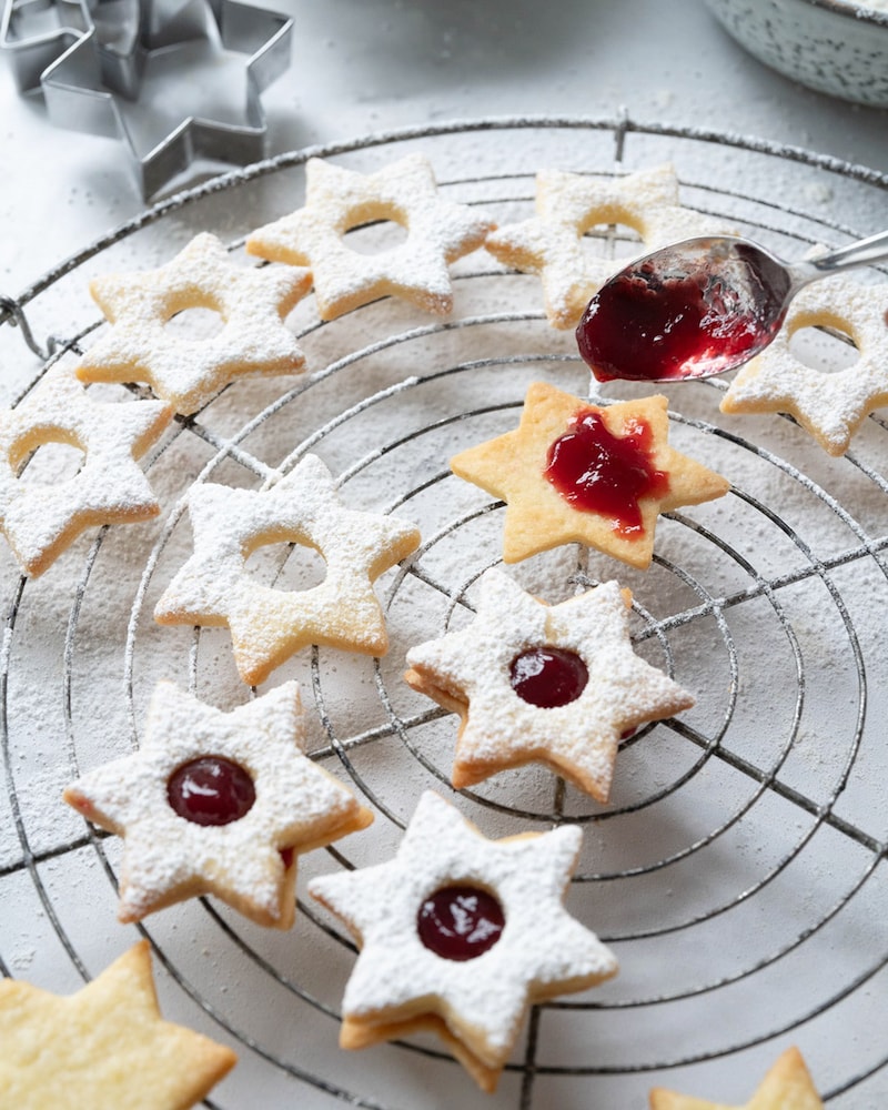 Dieses Bild zeigt wie die eine Hälfte der Sterne mit Himbeeren Konfitüre bestrichen wird.