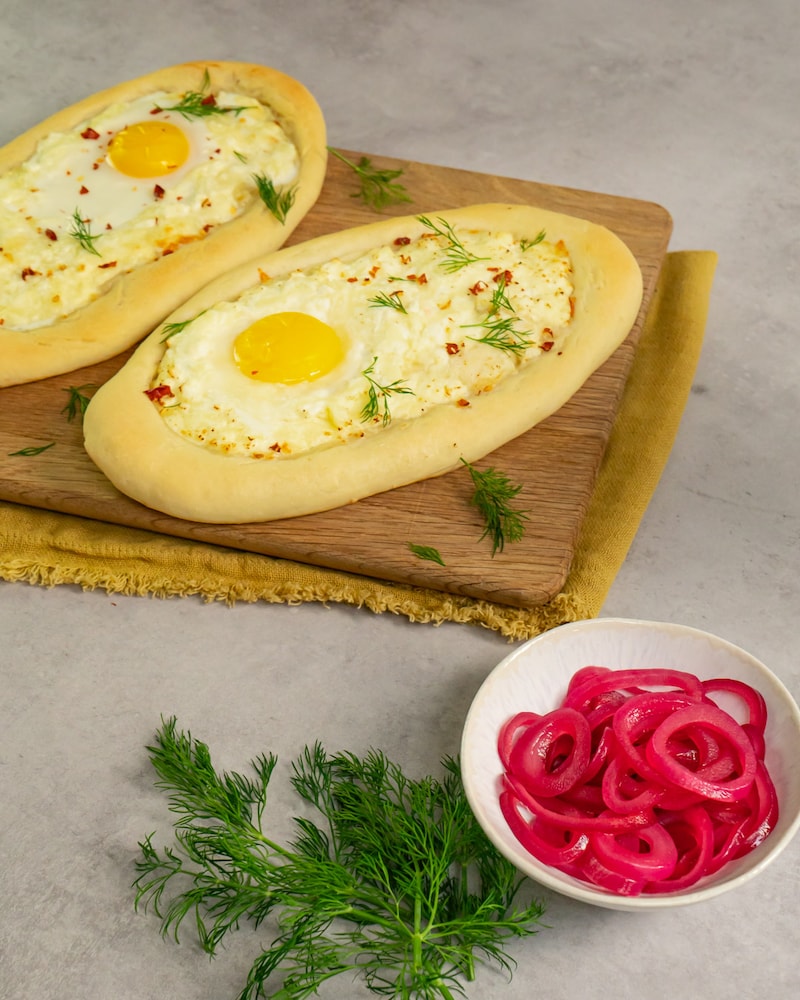 Dieses Bild zeigt die fertigen Khachapuri wie sie noch mit den Zwiebeln belegt werden.