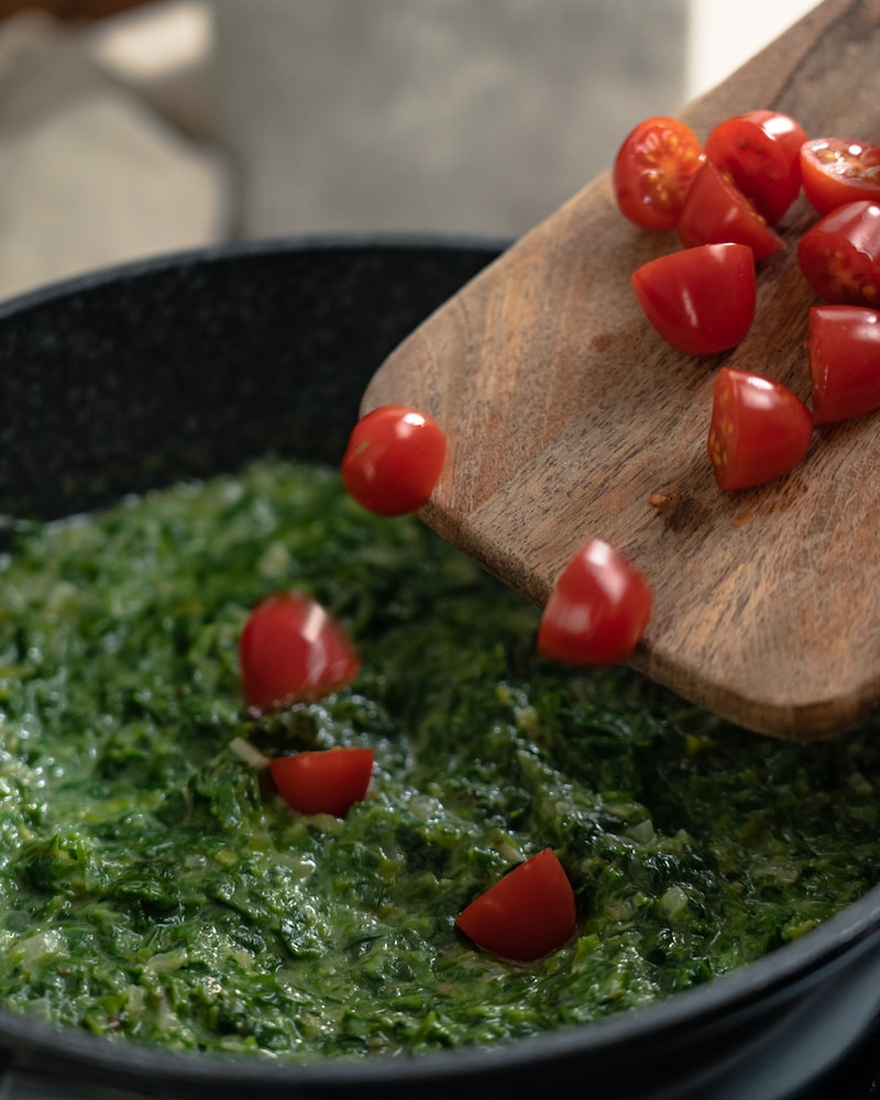 Auf diesem Bild siehst du wie Tomaten zum Spinat gegeben werden.