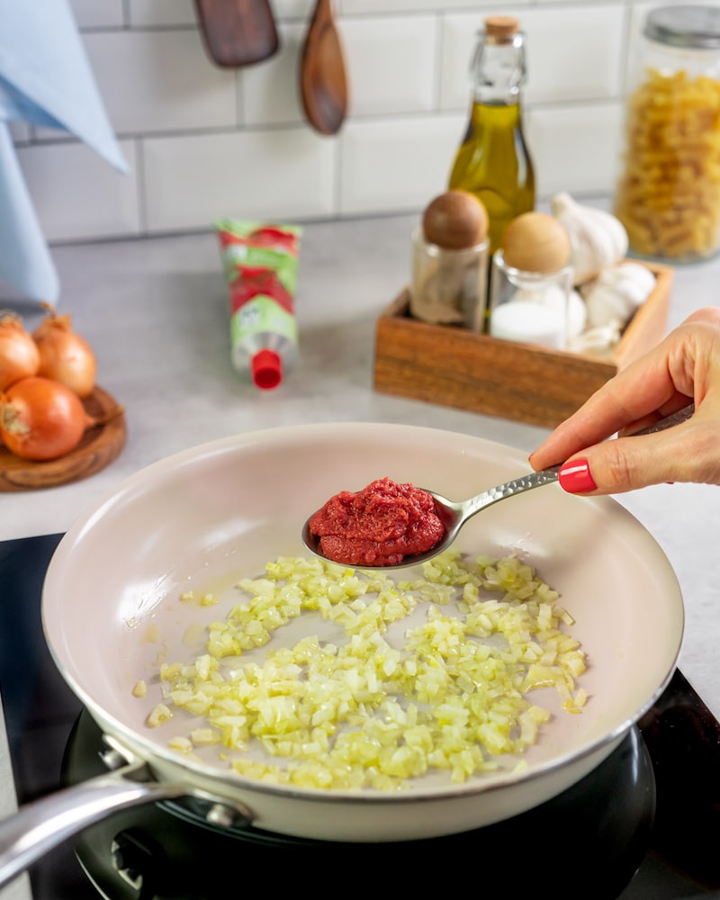 Dieses Bild zeigt wie Tomatenmark zu den Zwiebeln gegeben wird.