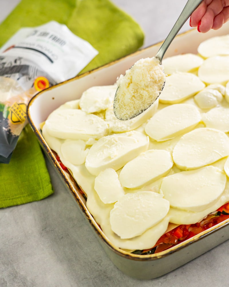 Dieses Bild zeigt wie der Käse über die Lasagne gegeben wird.