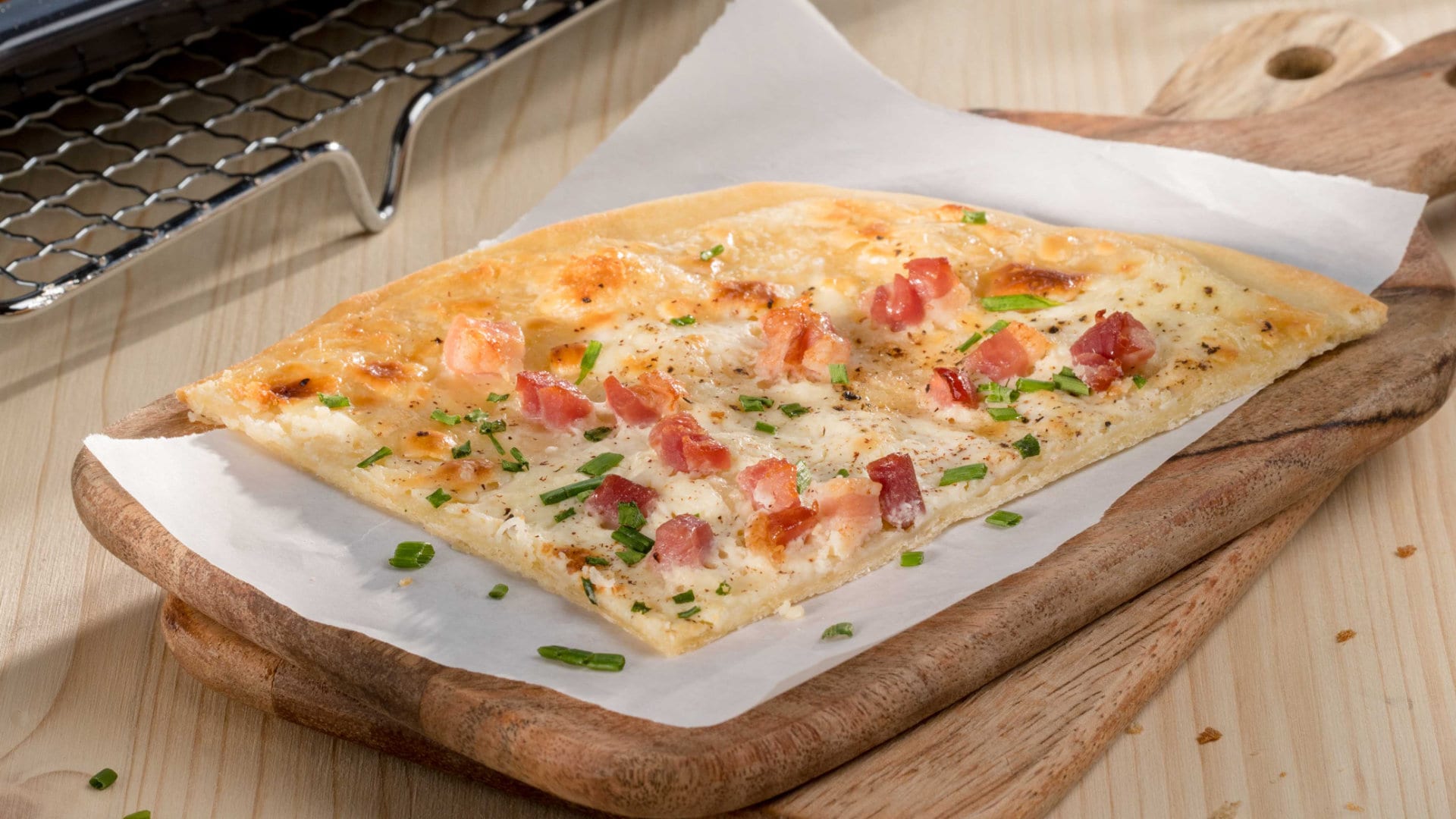 Flammkuchen mit Speck auf einem Holzbrett.