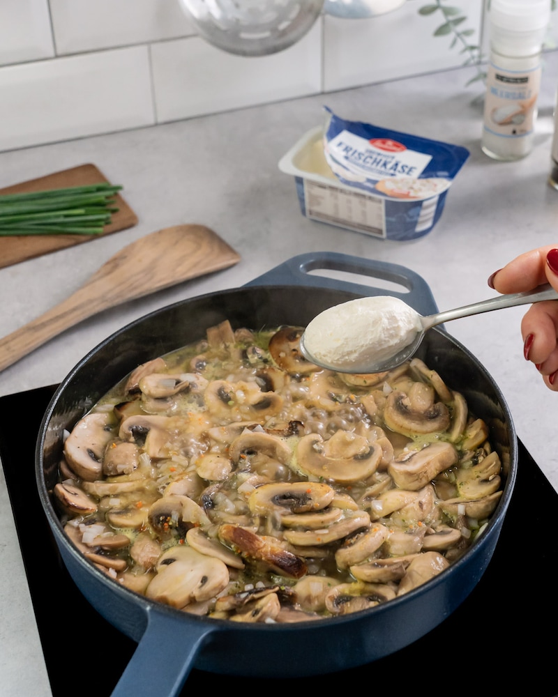 Diese Bild zeigt wie der Frischkäse zu der Pilzen gegeben wird.