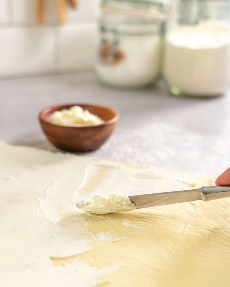 Dieses Bild zeigt wie der Pizzateig mit Frischkäse bestrichen wird.
