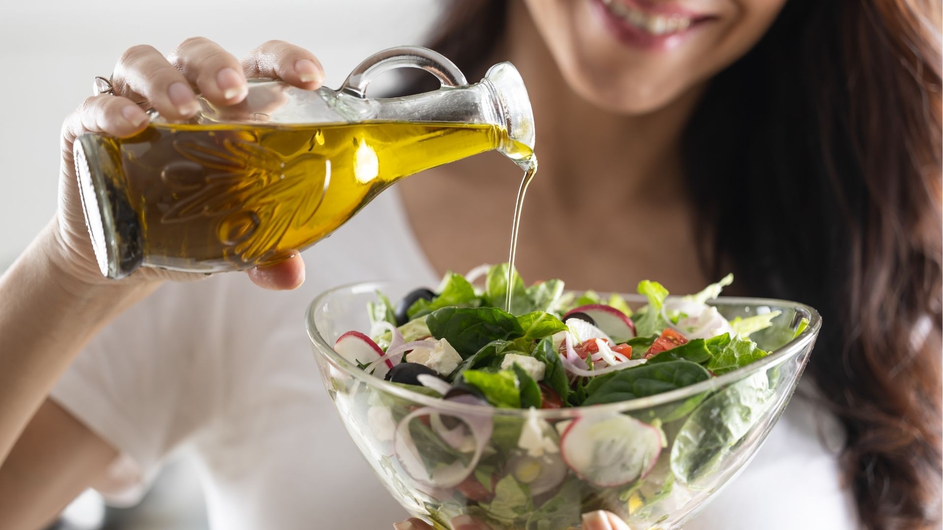 Frau fügt Öl zu Salat hinzu