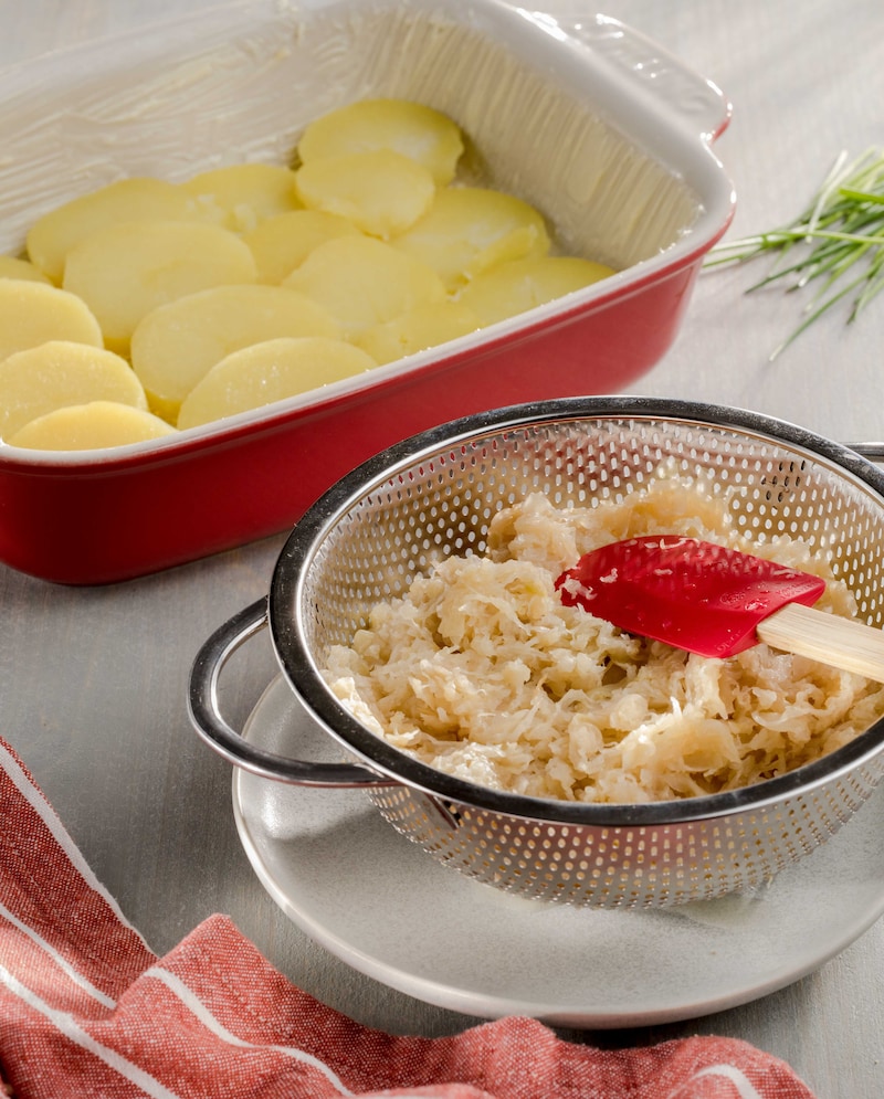Auf diesem Bild siehst du Sauerkraut und eine Auflaufform mit Kartoffelscheiben.
