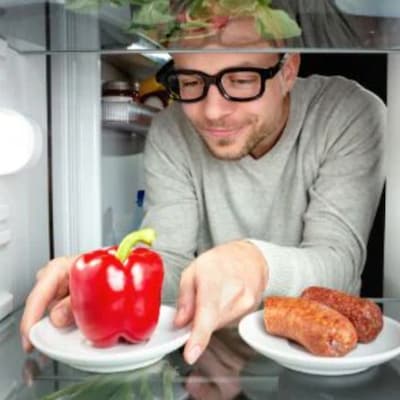 Mann, der Paprika statt Wurst aus Kühlschrank nimmt