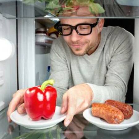 Mann, der Paprika statt Wurst aus Kühlschrank nimmt