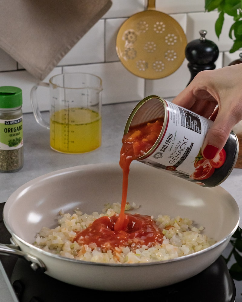 Dieses Bild zeigt wie die Tomatensoße zu den Zwiebeln gegossen wird.