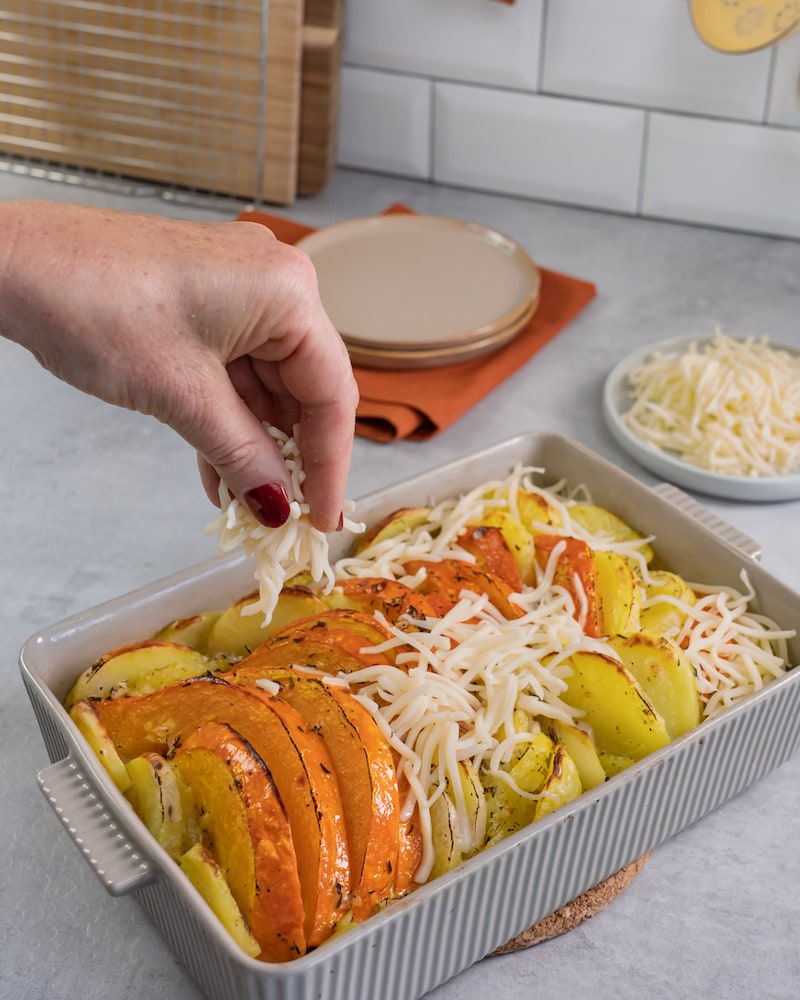 Dieses Bild zeigt wie der Käse über den Kürbis und die Kartoffeln gegeben wird.