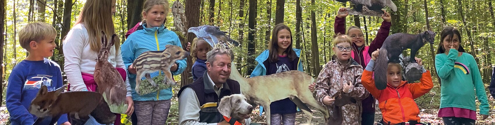 Kindergruppe steht im Wald mit Papierfiguren