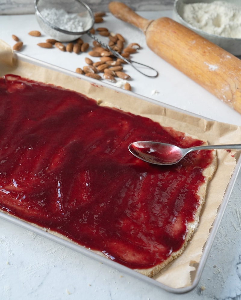 Dieses Bild zeigt wie der Teig für die Linzer Streifen ausgerollt und mit Konfitüre bestrichen wird.