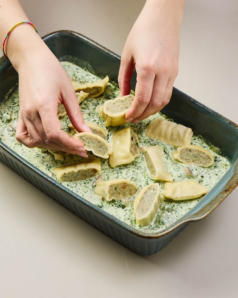 Dieses Bild zeigt, wie die Maultaschen auf der Mischung in einer Ofenform verteilt werden.