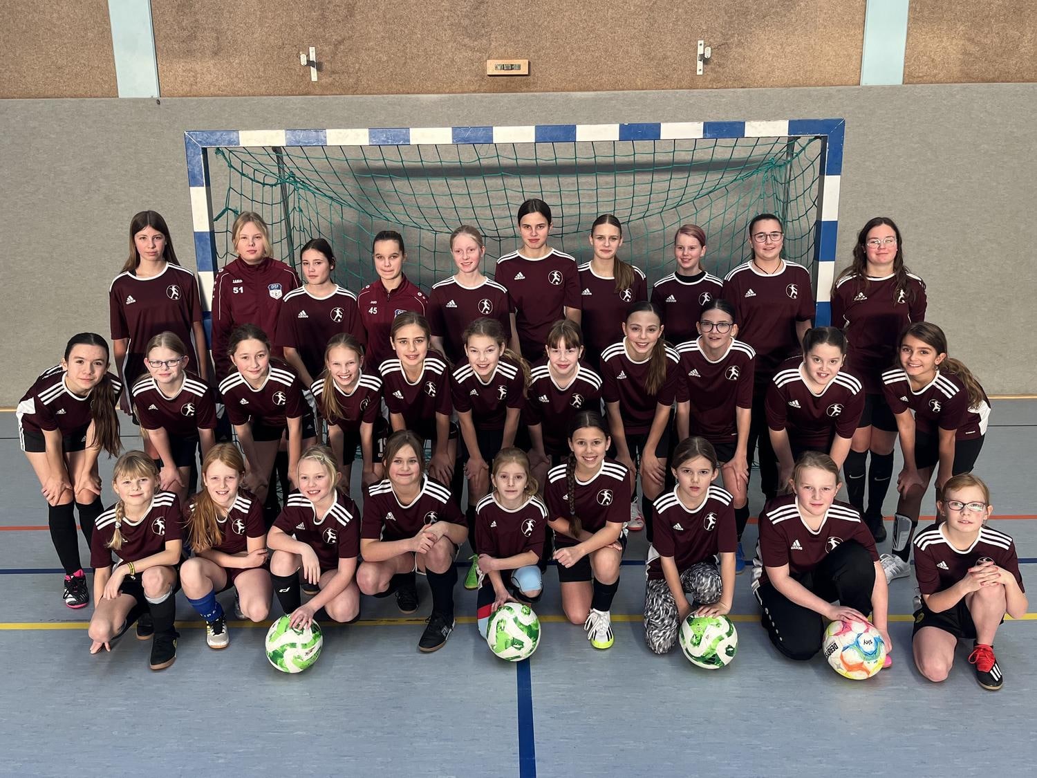 Maedchen sind versammelt auf dem Spielfeld und laecheln in die Kamera