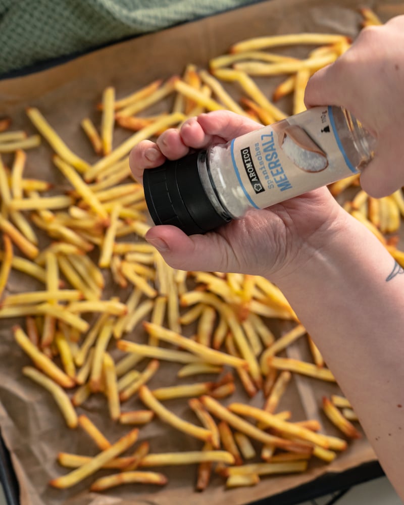 Auf diesem Bild siehst du wie die Pommes gesalzen werden.