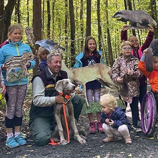 Kindergruppe steht im Wald mit Papierfiguren