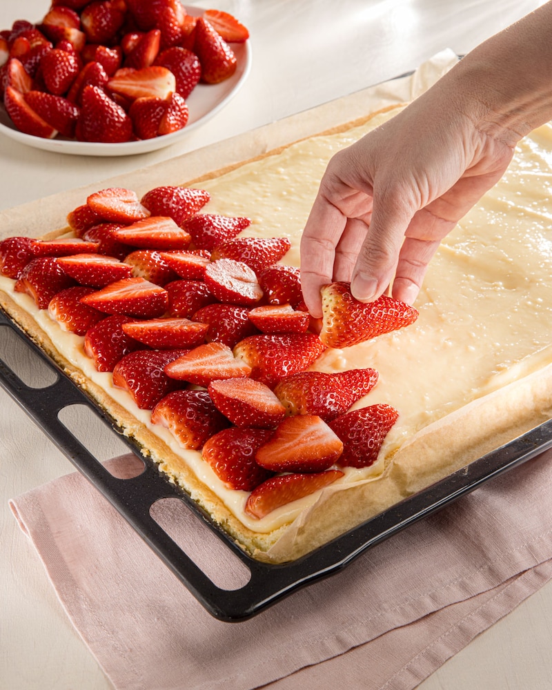 Dieses Bild zeigt wie die Erdbeeren auf den Kuchen gegeben werden.