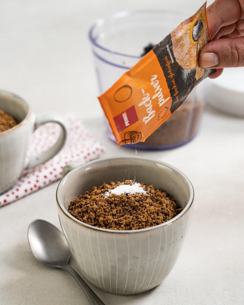 Auf diesem Bild siehst du wie Backpulver auf die zerkrümelten Cookies gegeben wird.