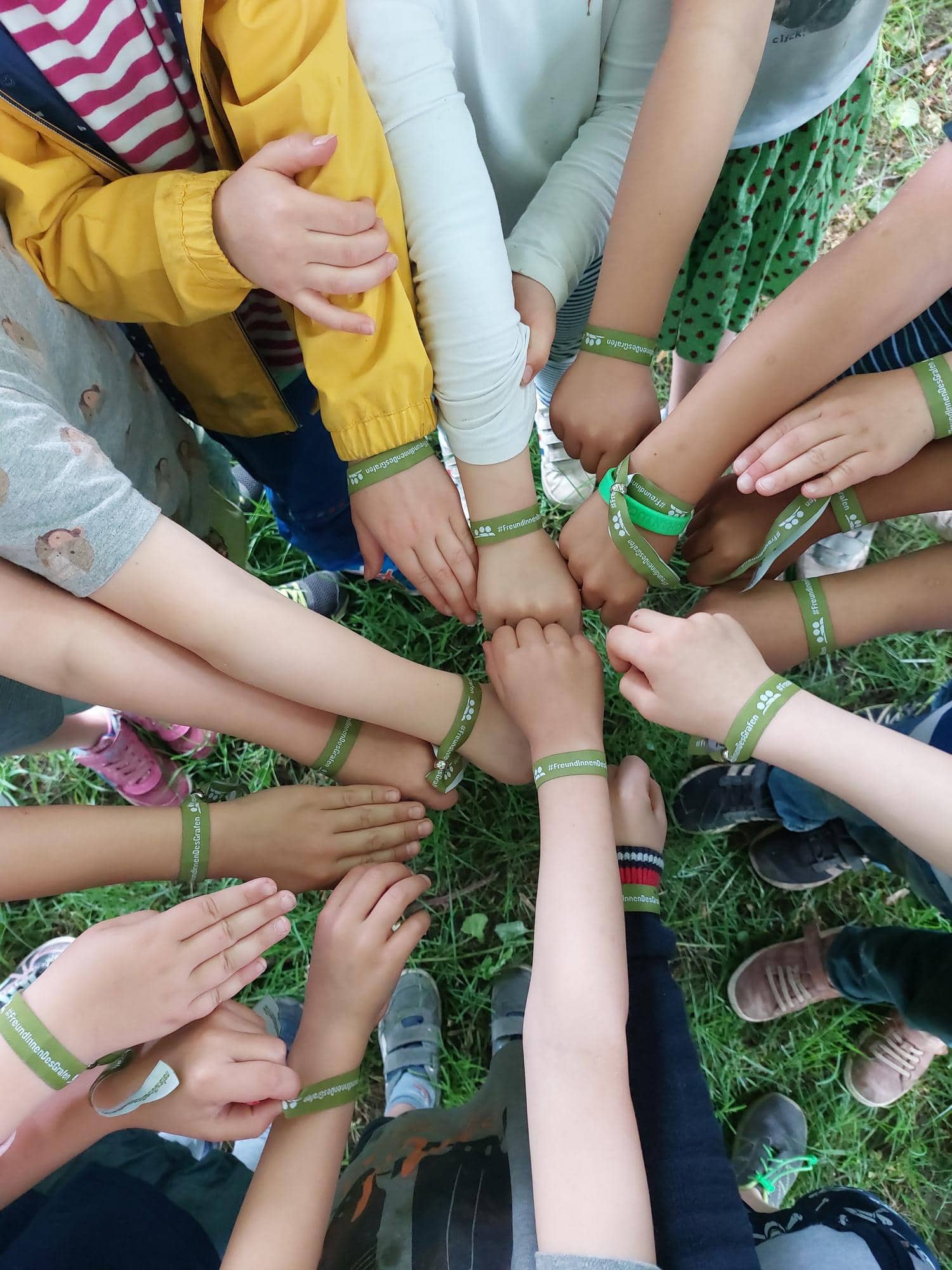 Kinder stehen in einem Kreis und strecken ihre Haende in die Mitte