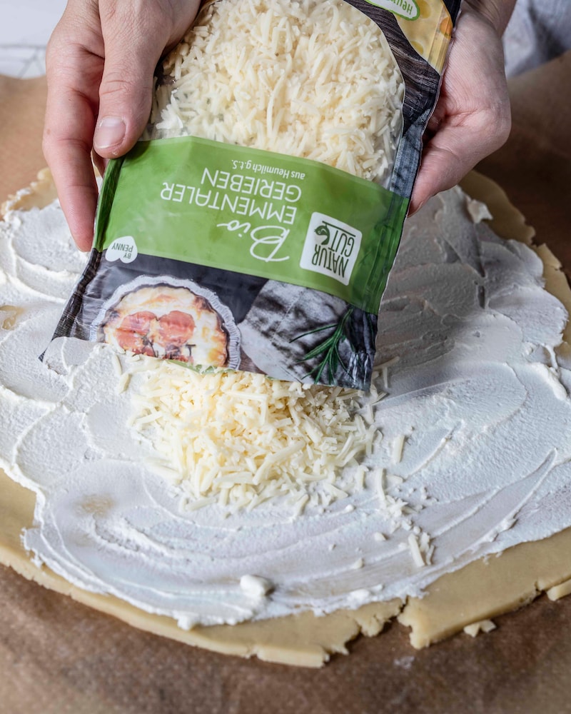 Dieses Bild wie der Käse auf die Galette gegeben wird.