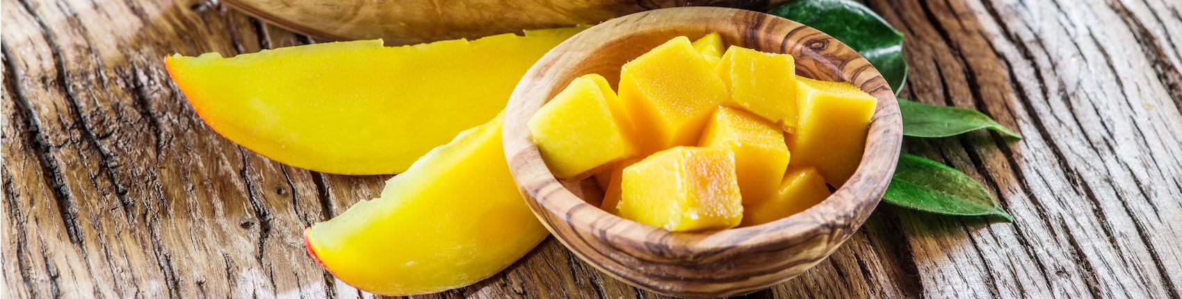 Gewürfelte Mango in Bambusschale auf einem braunen Holztisch.